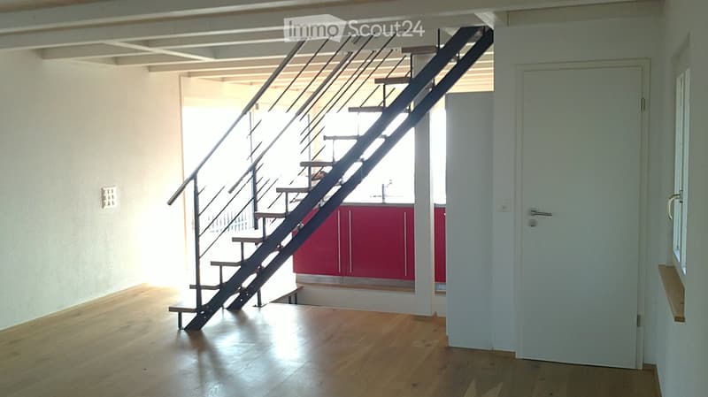 Modern hallway with wooden flooring, white walls, and a staircase leading to an upper level. The staircase features a metal railing and wooden steps. A red cabinet is visible in the background.