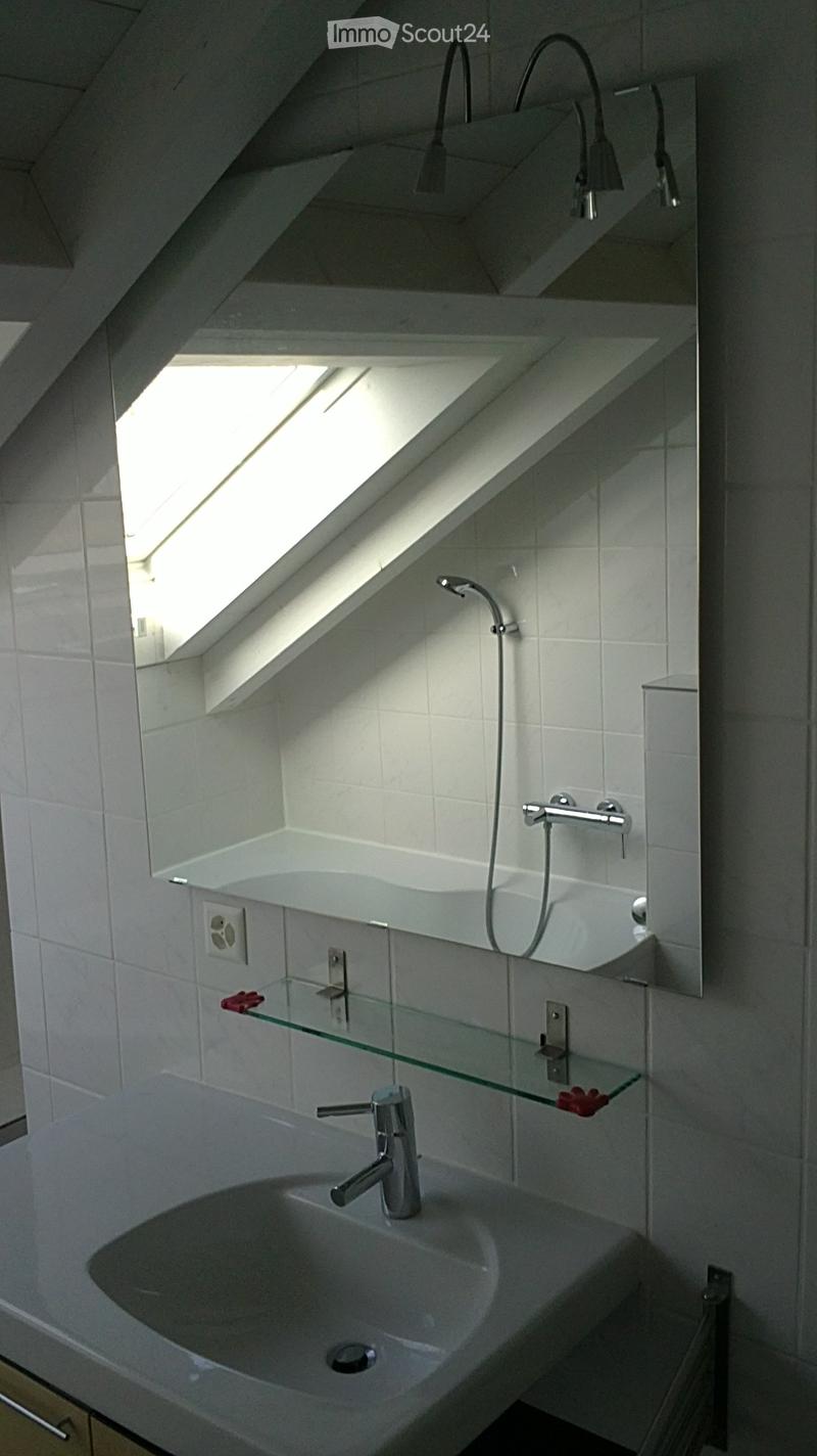 Modern bathroom with a white tiled wall, a large mirror, a sink with a chrome faucet, a bathtub, and a glass shelf with red decorative items.