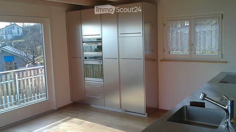 Modern kitchen with light-colored cabinets, a stainless steel sink, and a view of the garden through large windows.