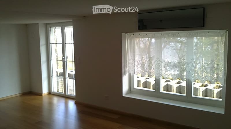 Empty room with wooden flooring, large sliding glass doors, and white curtains. No furniture or equipment present.