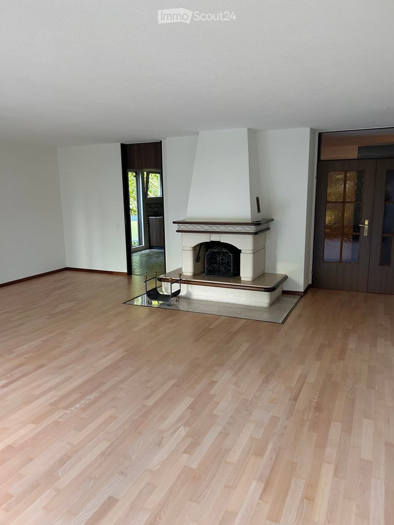 Empty room with light wooden flooring, white walls, and a fireplace with a decorative mantel and black iron grate.
