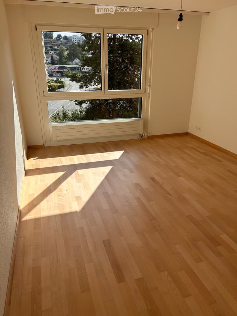 Empty room with light wooden flooring, large windows, and a radiator under the windows.