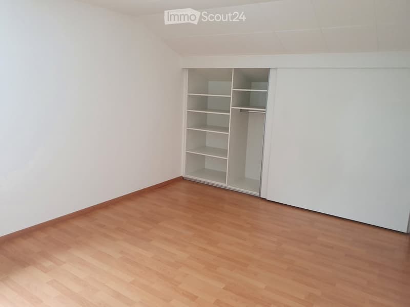 Empty room with wooden flooring and white walls, featuring an open closet with empty shelves and hanging space.