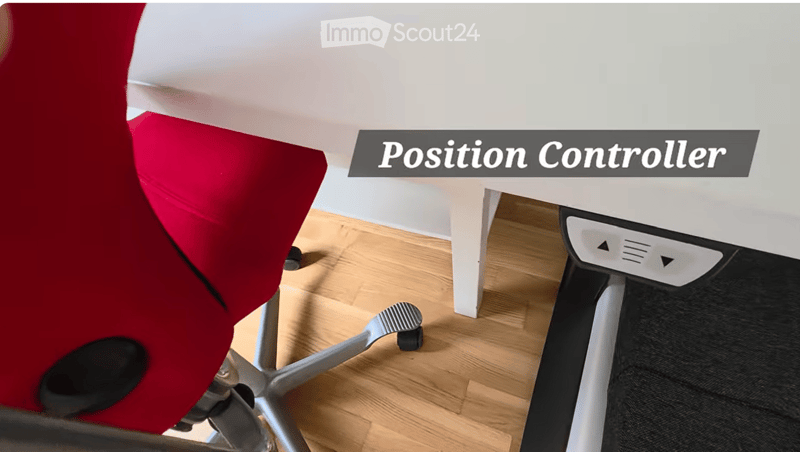 A modern office setup featuring a red ergonomic chair and a white desk with a position controller device.