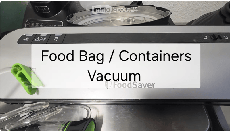 A food saver vacuum machine with a food bag attached, featuring various control buttons and a stainless steel container on top.