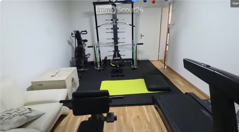 A well-equipped home gym with a white sofa, exercise bike, weight machine, barbell, yoga mat, foam roller, and storage box.