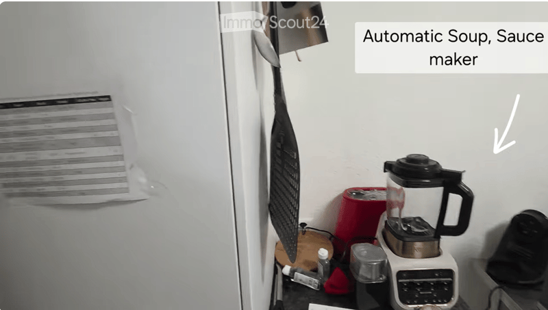 A modern kitchen with a blender, toaster, and a refrigerator. The countertop is clean and organized, with a bottle and a faucet visible.