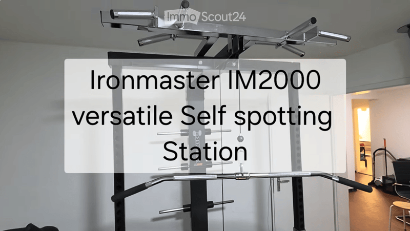 A modern fitness room with a versatile self-spotting station, featuring a large metal frame with multiple bars and weights, and a small wooden stool in the background.