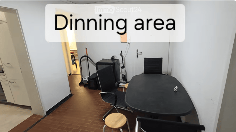 Dining area with a black dining table, chairs, a small wooden stool, and a refrigerator in the background.