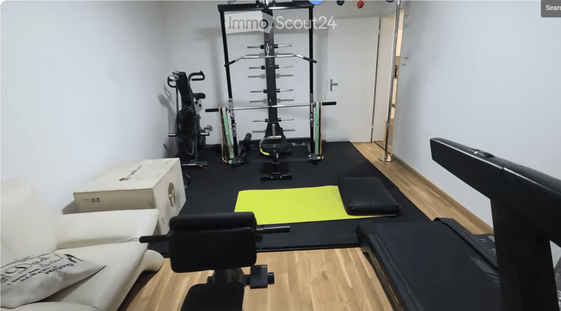 A well-equipped home gym with a sofa, exercise bike, weight machine, yoga mat, and cushion.