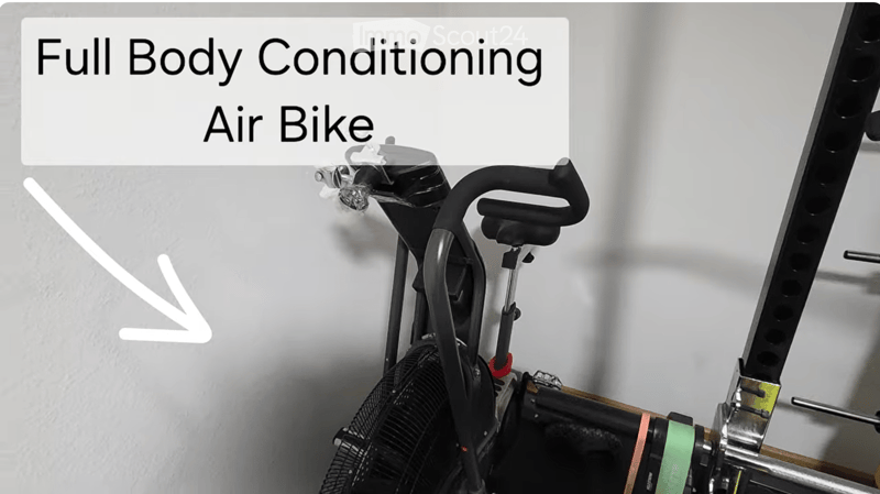 An air bike exercise machine is mounted on a wall, featuring a handlebar, seat, and fan-like resistance system.