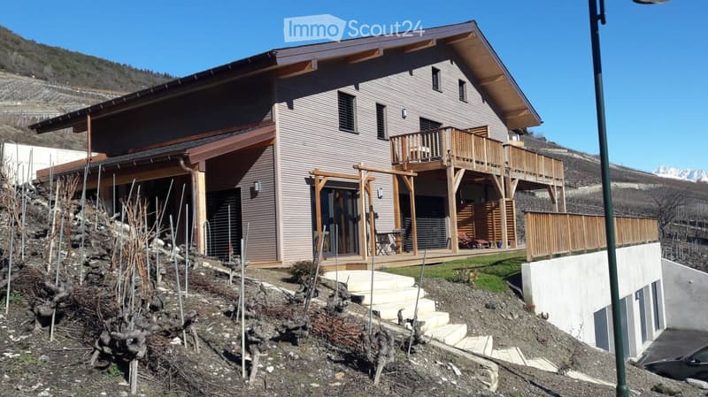 Two-story modern house with wooden balconies, large windows, and a scenic mountain view in the background.