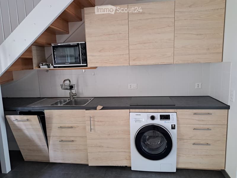 Modern kitchen with light wood cabinets, stainless steel appliances, and a black countertop.