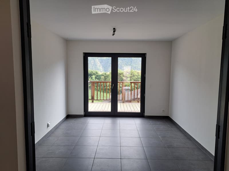 Empty room with tiled floor, white walls, and a large sliding glass door leading to a wooden deck with a scenic view.