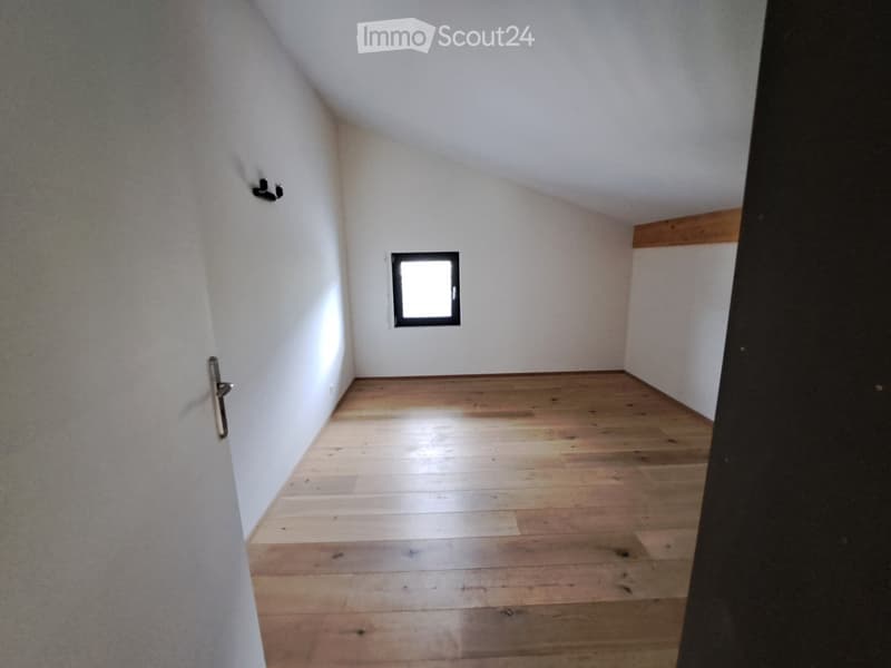 Empty room with wooden flooring, white walls, and a small window letting in natural light. The room has a simple, clean design with no furniture or decorations.