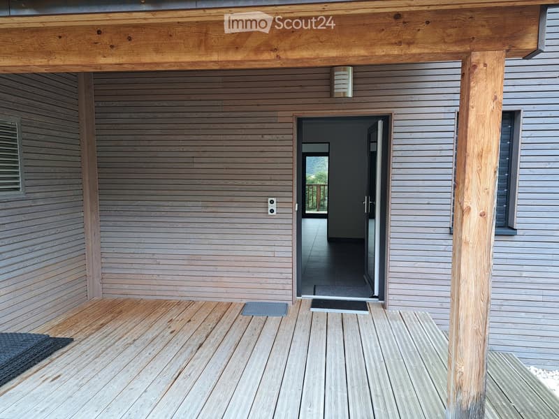 Wooden deck with grey siding walls, entrance door, and a small mat.