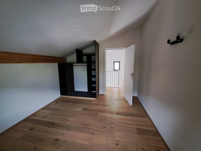 Empty hallway with wooden flooring, white walls, and an open door leading to another room.
