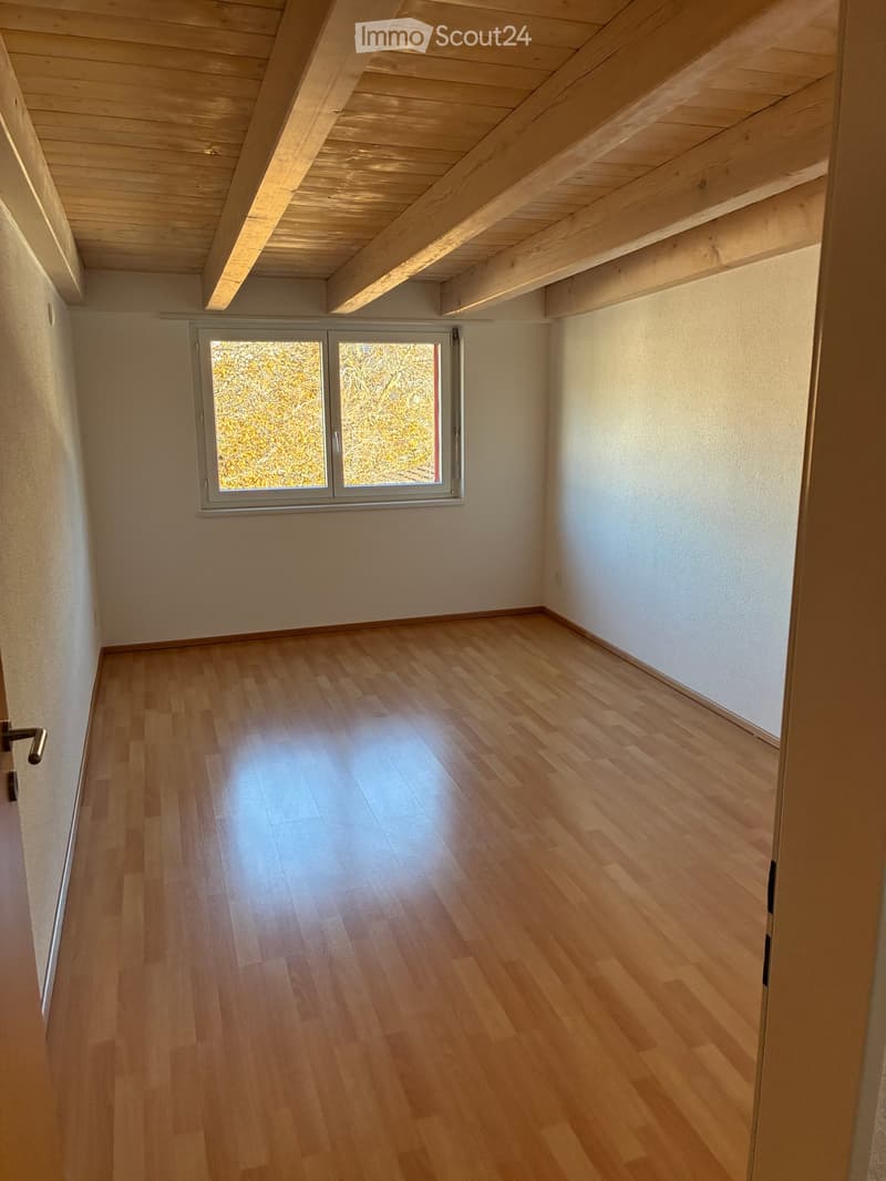Empty room, hardwood floor, wooden beams, white walls, single window, wall mounted power outlets