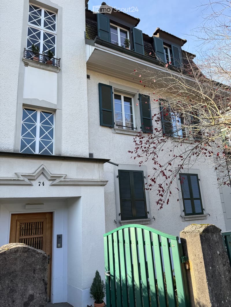 Two-story house, white exterior, black shutters, balcony with plants, wooden door, green gate