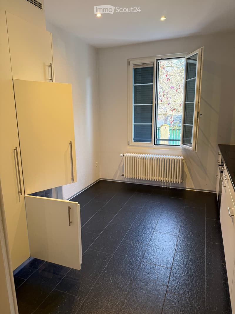 empty room with white walls, black floor tiles, white ceiling, window with white shutters, a white radiator, and open cabinets