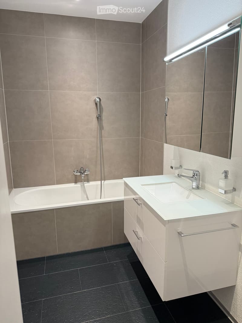 modern bathroom with bathtub, vanity unit, and tiled walls