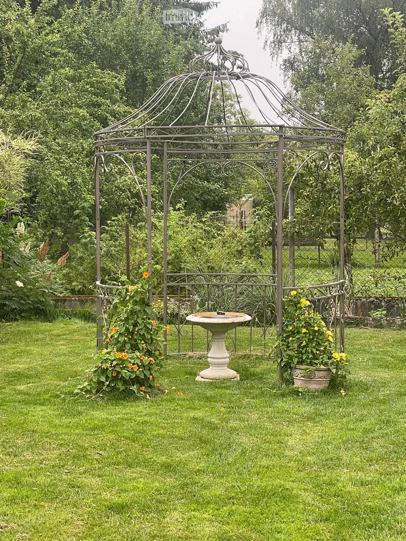 Garden with a metal gazebo, a stone fountain, and potted plants with yellow flowers.
