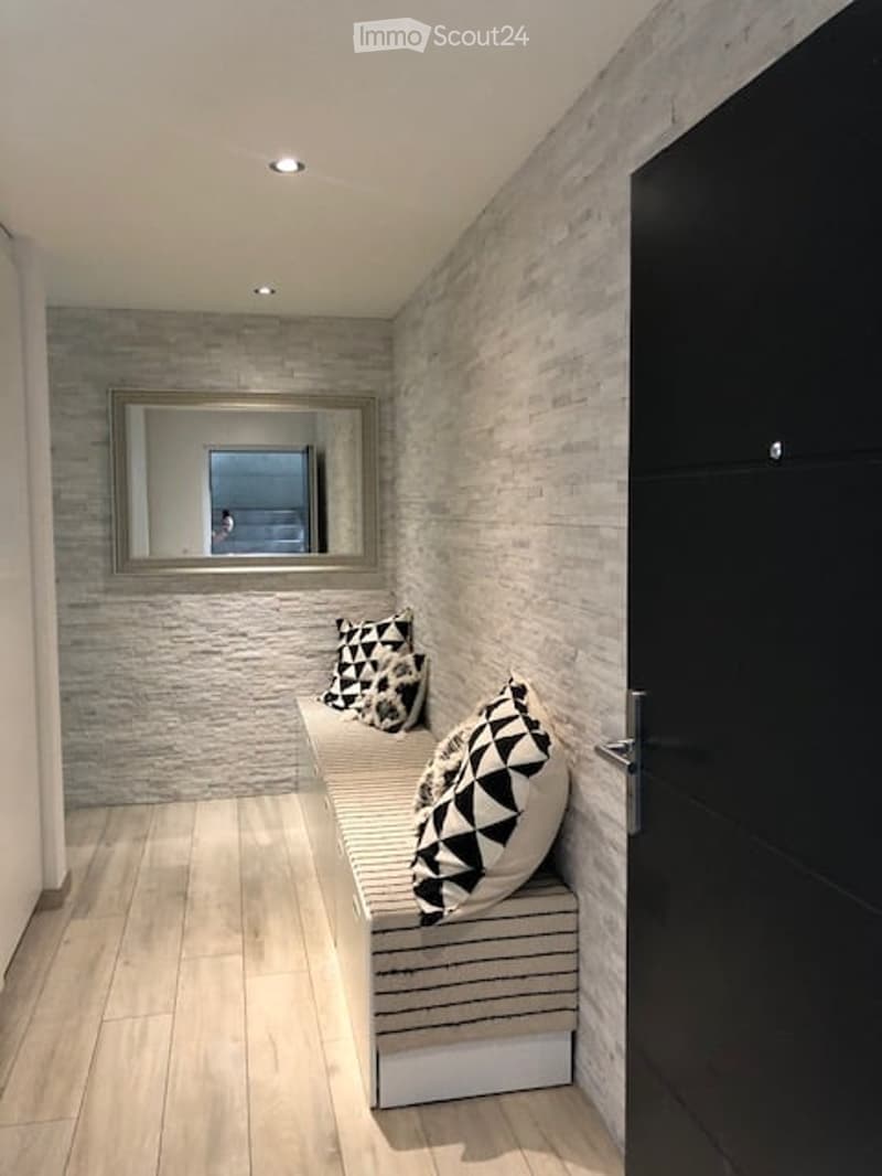 A modern, narrow hallway with a built-in bench featuring geometric patterned pillows, a large mirror on the wall, and recessed lighting.
