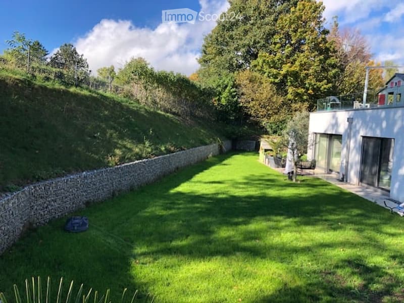Well-maintained garden with a raised stone wall on one side, a modern white house with large windows, and a small seating area with a table and chairs.