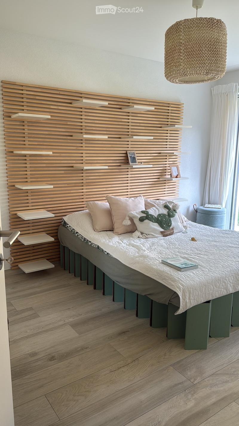 Modern bedroom with a wooden bed frame, decorative pillows, a woven hanging lamp, and built-in wooden shelves behind the bed.