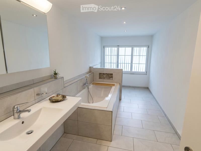 Modern bathroom with a large bathtub, double sink, and a decorative plant on the counter.