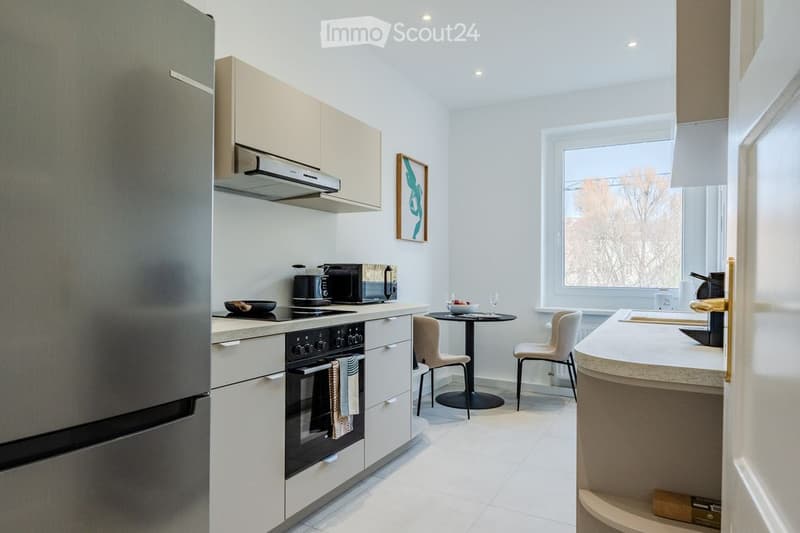 Modern kitchen with white cabinets, stainless steel appliances, a kitchen island, and a small dining area with a table and chairs.