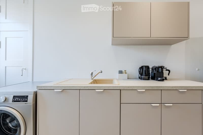 Modern kitchen with white cabinets, a sink, a coffee maker, and a washing machine.