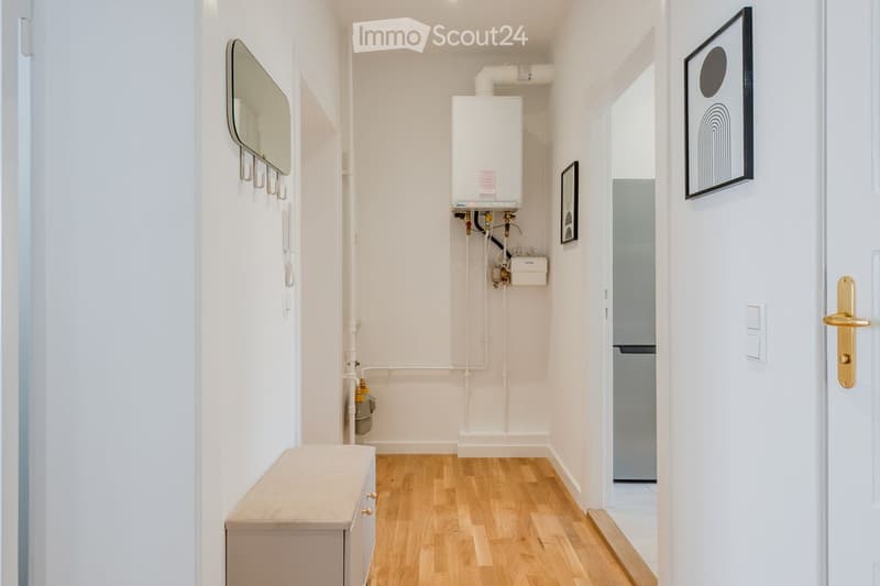 Narrow hallway with light wooden flooring, white walls, a small bench, a mirror, and a water heater unit mounted on the wall.