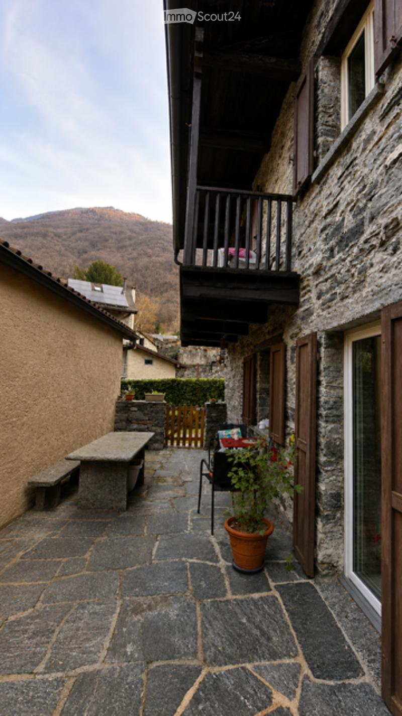 Courtyard with stone pavement, small seating area, potted plant, and a balcony overlooking the area.