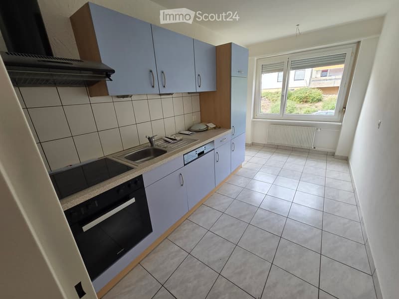 Modern kitchen with light blue cabinets, tiled walls, and a window overlooking a garden. Features include a sink, oven, dishwasher, and range hood.