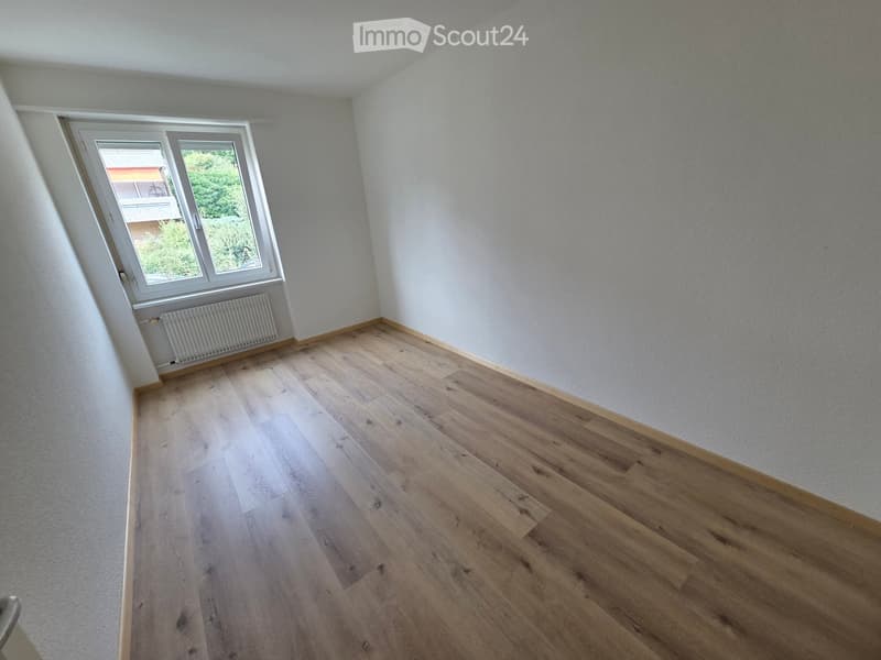 Empty room with light wooden flooring, white walls, and a window with a radiator below it.