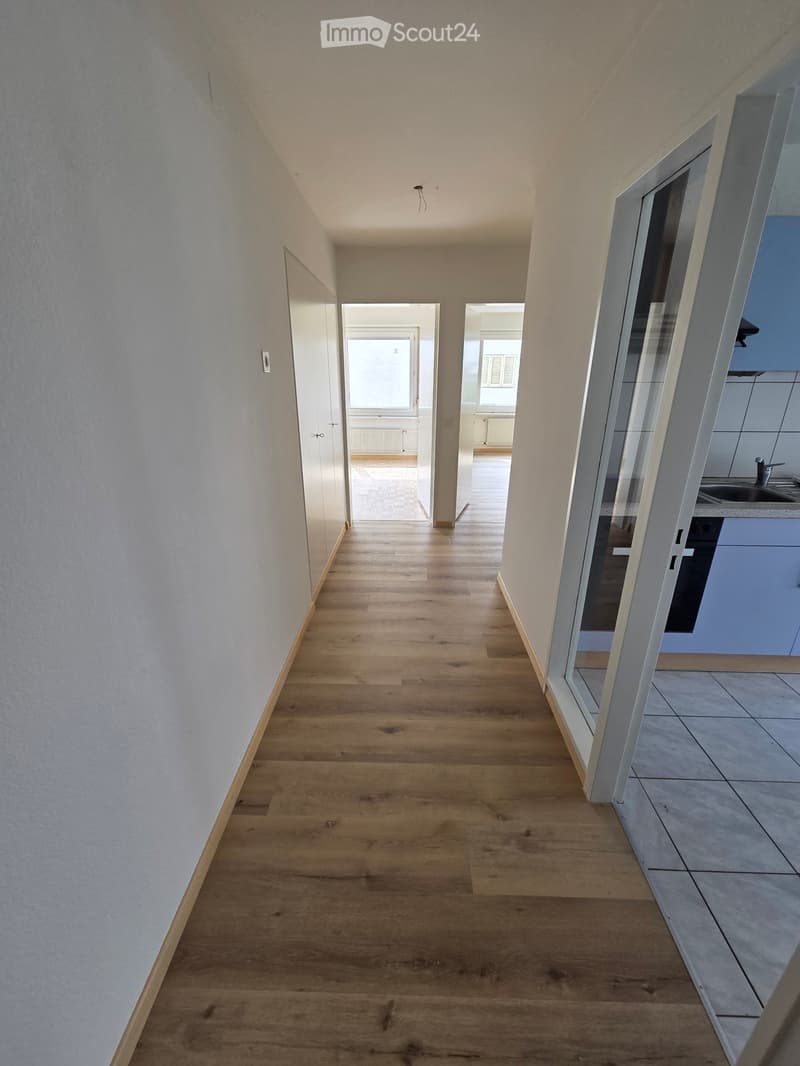 Empty hallway with wooden flooring, white walls, and doors leading to other rooms.