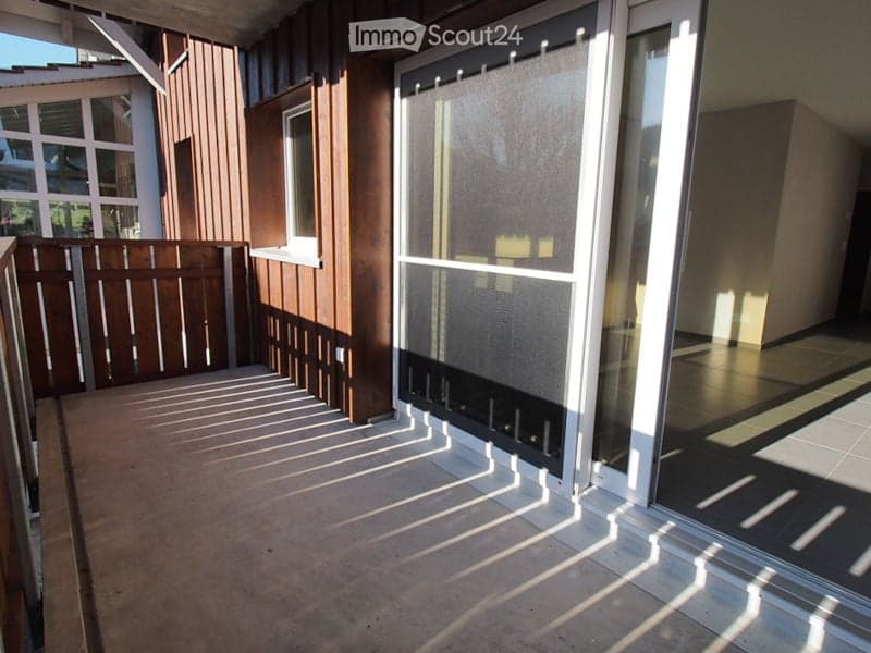 Balcony with wooden railing, large sliding glass doors, and a view of the surrounding area.