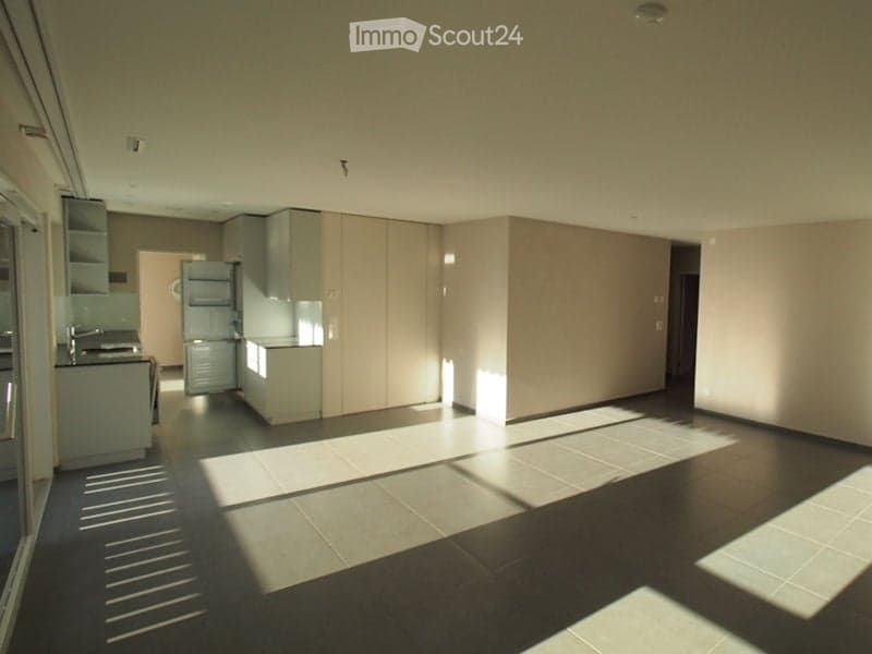 Open-plan unfurnished room with modern cabinetry, tiled floor, and natural light from large windows. No furniture or equipment present.