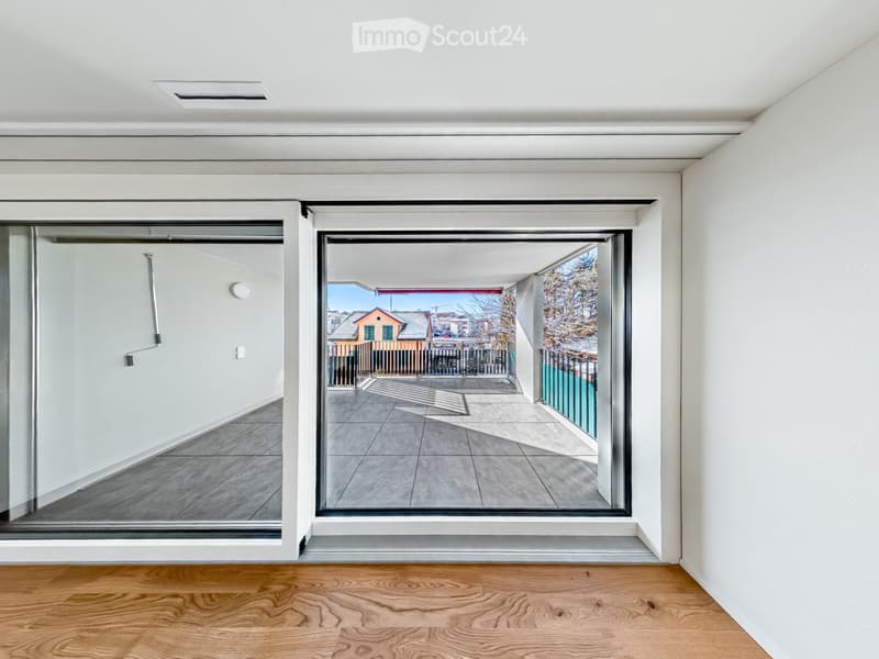 Empty room with wooden flooring, white walls, and large sliding glass doors leading to a balcony with a tiled floor and metal railing.