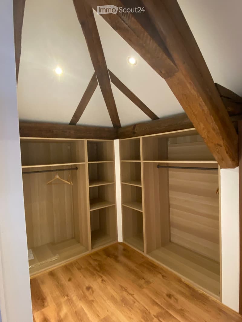 Empty attic space with wooden beams, built-in wooden shelving units, and wooden flooring.