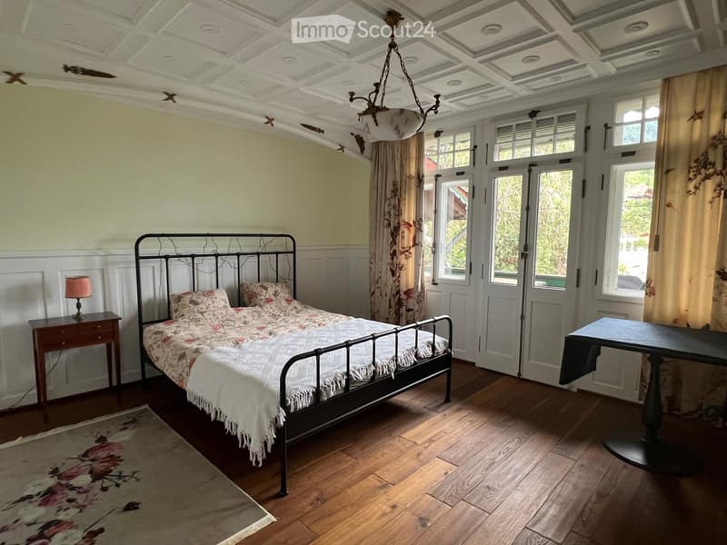 Cozy bedroom with wooden floors, a metal-framed bed with floral bedding, a nightstand with a lamp, a small table, and a decorative rug.