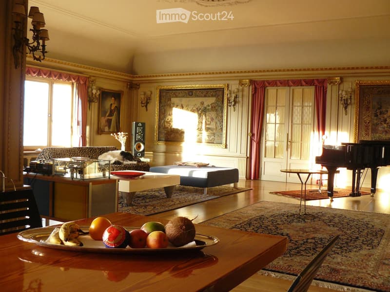 Elegant living room with large windows, ornate curtains, a sofa, coffee table, piano, and fruit bowl on a wooden table.