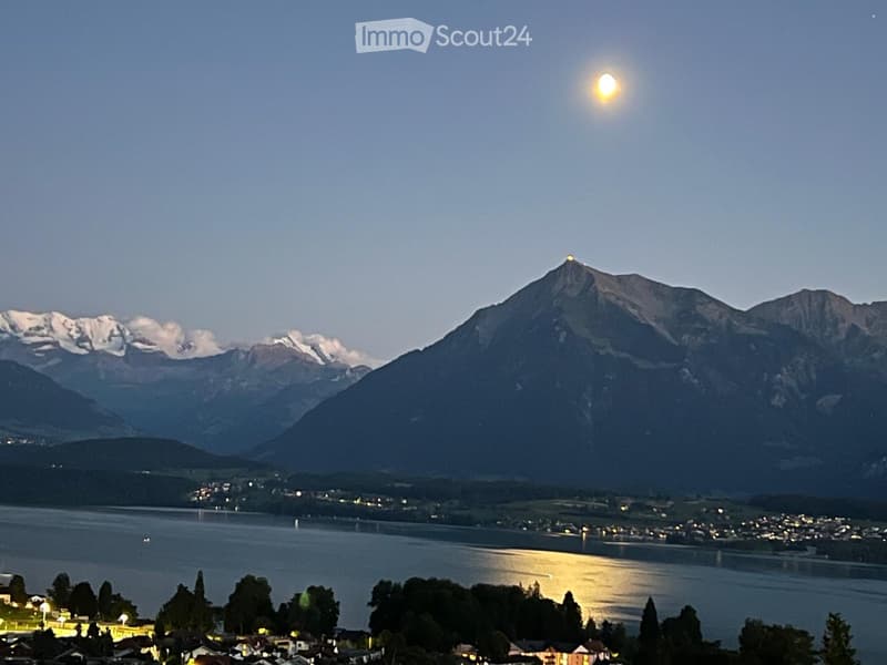 A serene lakeside view with snow-capped mountains in the background, illuminated by the setting sun, with a small town visible along the shoreline.