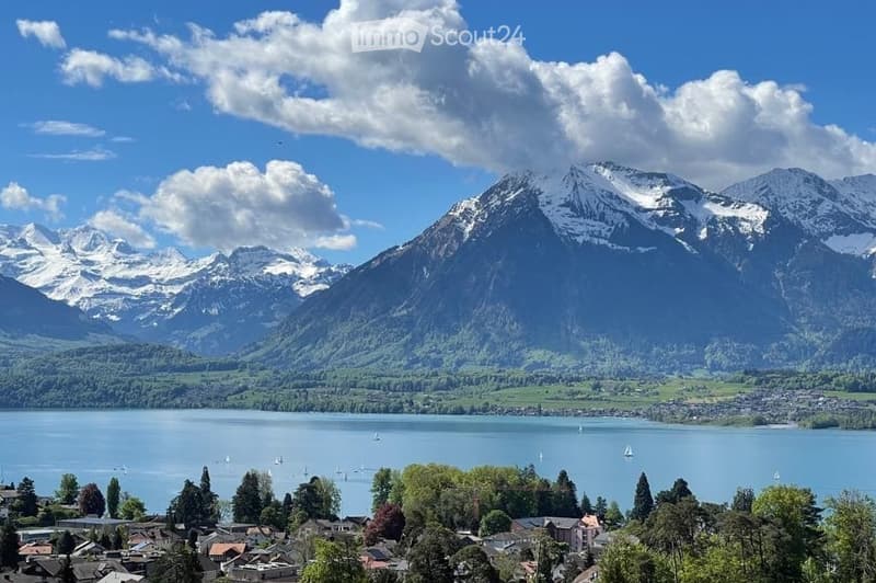 Panoramic view of a serene lake surrounded by snow-capped mountains, with a small town visible along the shoreline.