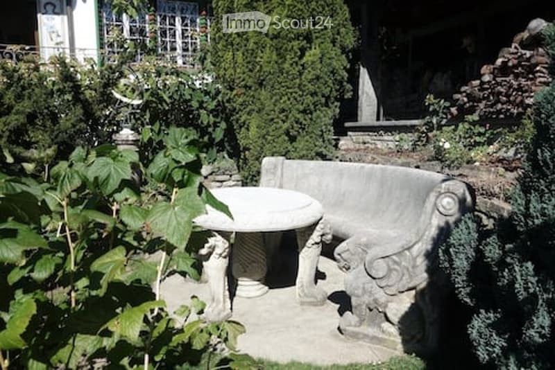 Garden area with a stone bench, a small round table, and lush greenery.