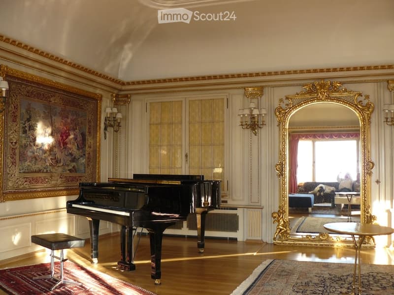 Elegant room with a grand piano, ornate mirror, and decorative wall sconces. The space features wooden flooring, large windows, and classic artwork.