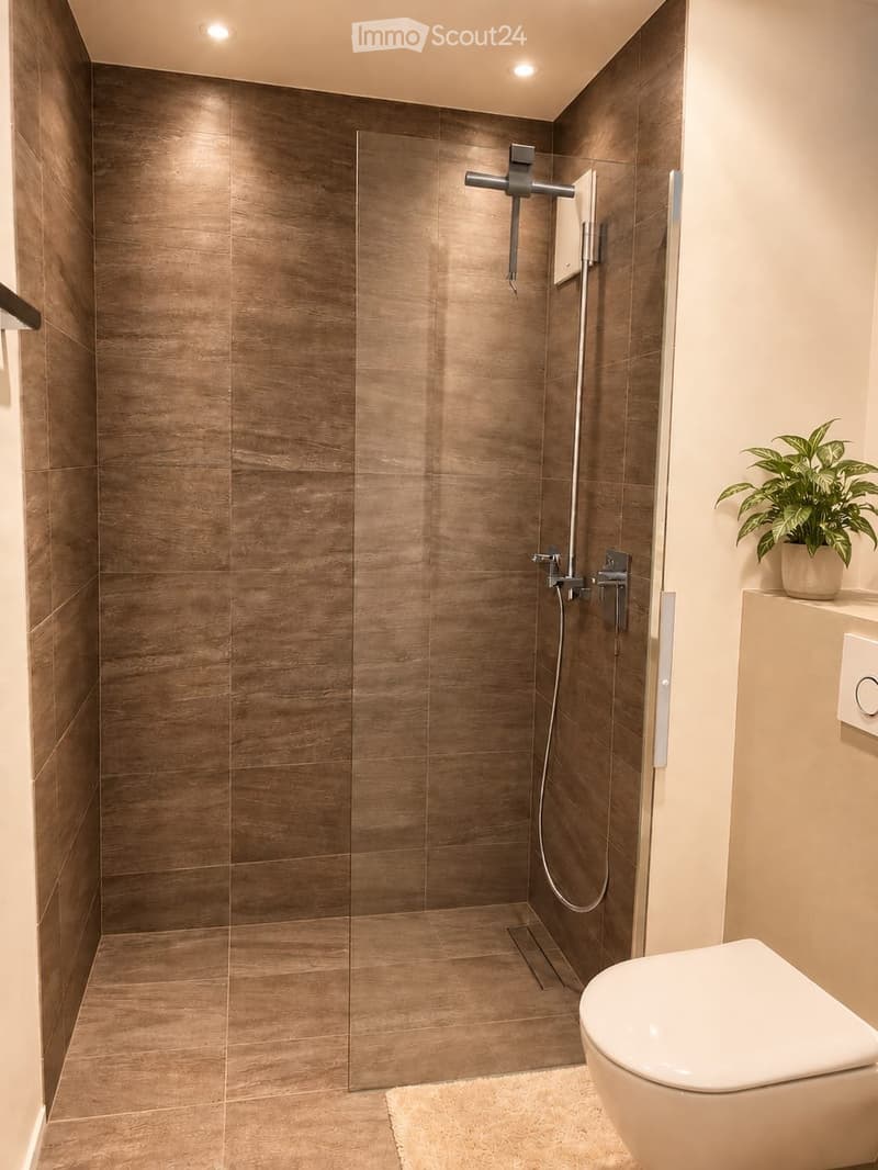 Modern bathroom with a glass-enclosed shower, sleek brown tiles, a white toilet, and a small potted plant on a shelf.