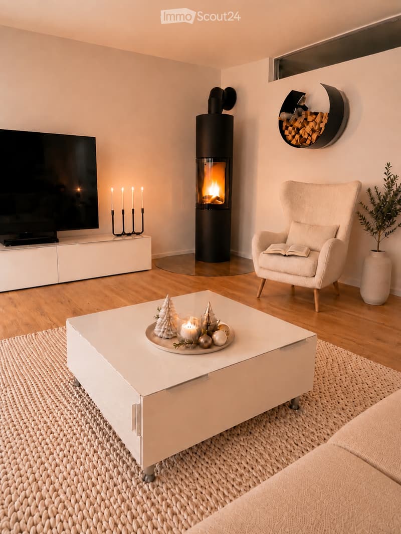 Modern living room with a fireplace, a white sofa, a coffee table with holiday decorations, an armchair, a television, and a decorative candle holder.