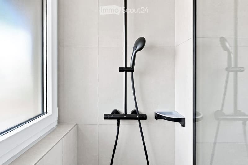 Modern bathroom shower area with a sleek black showerhead mounted on a rail, a glass shower enclosure, and a small built-in shelf.